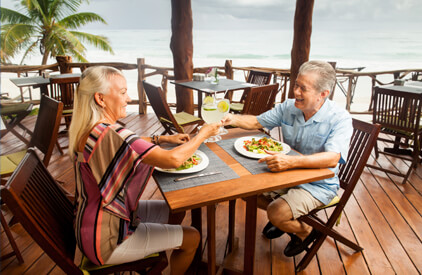 Older couple sitting across from each other on a tropical patio, toasting over dinner