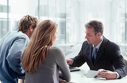 3 people sitting at a table looking at paperwork and a laptop. Two people with their back to the camera