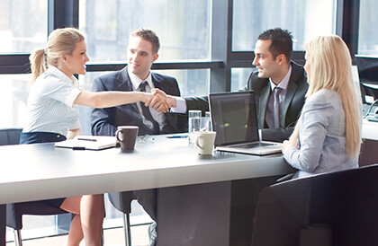 A group of business people, 2 men and two women. One man and one woman are shaking hands