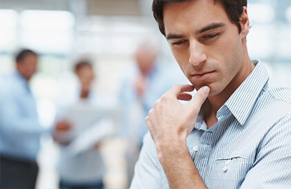 A man with his hand to his chin in a pondering expression. 3 more people are blurred in the background