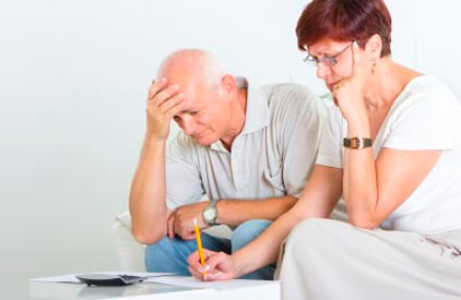 A man and a woman sitting beside each other reviewing paperwork with a calculator and pencil.