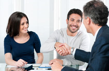 Happy couple sitting on a couch facing a 2nd man. The two men are shaking hands